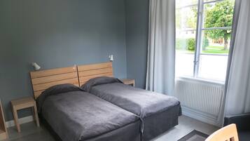 Een slaapkamer met een tweepersoonsbed, een nachtkastje, een stoel en een raam met gordijnen.