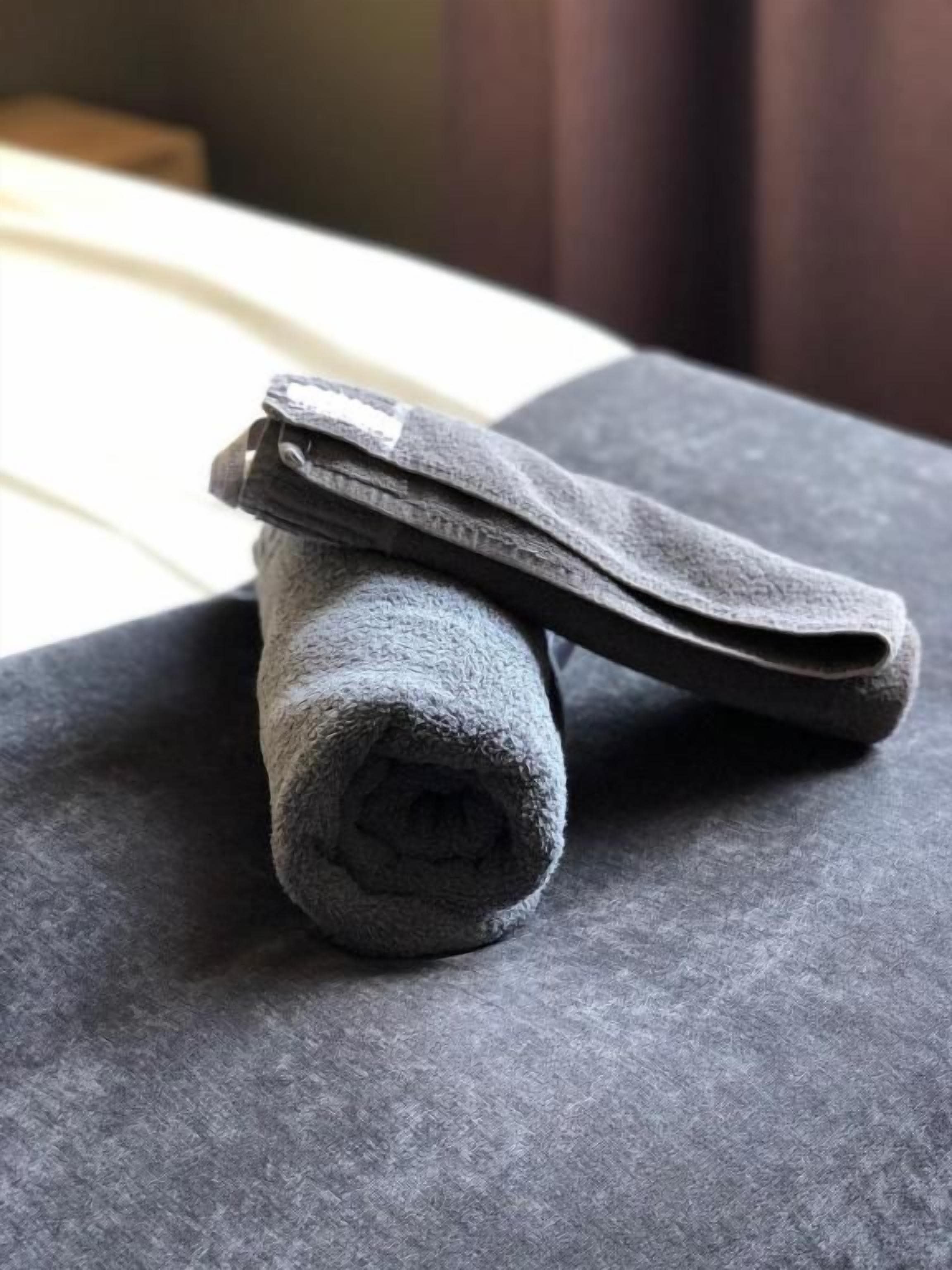 A rolled-up gray towel on a textured gray surface, possibly a bed or couch.