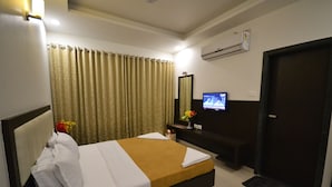 A hotel room with a bed, curtains, a TV, a mirror, and a door. - Hotel Dhantara (Rahata)