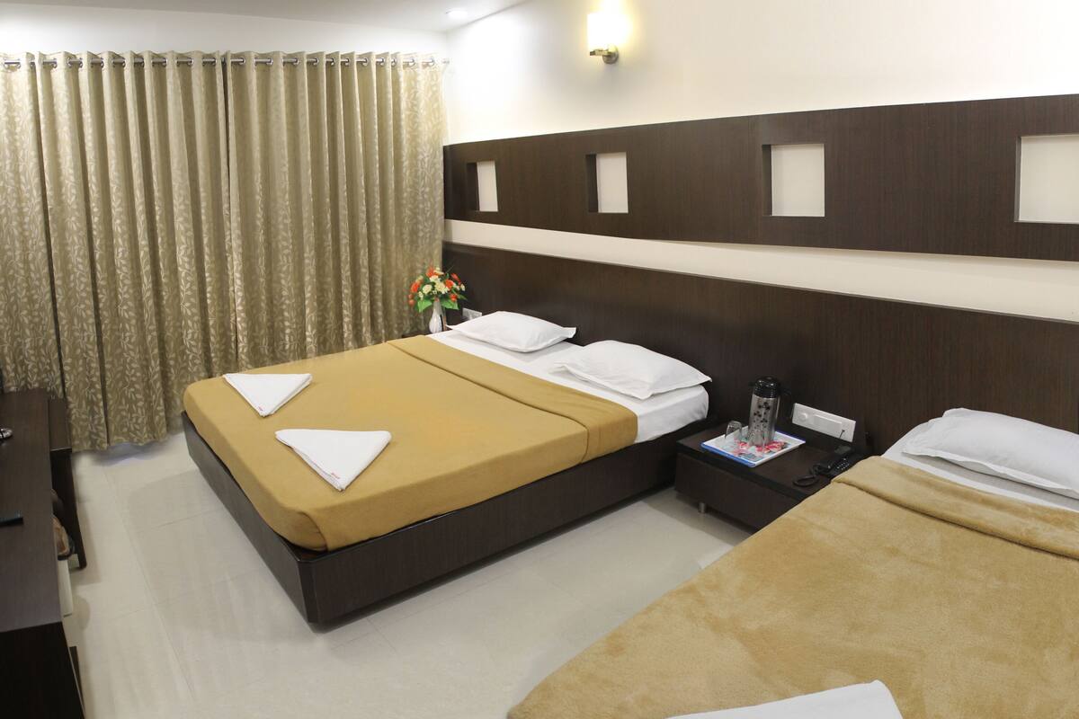 A hotel room with two single beds, a desk, a chair, a nightstand, and a bathroom with a shower curtain.