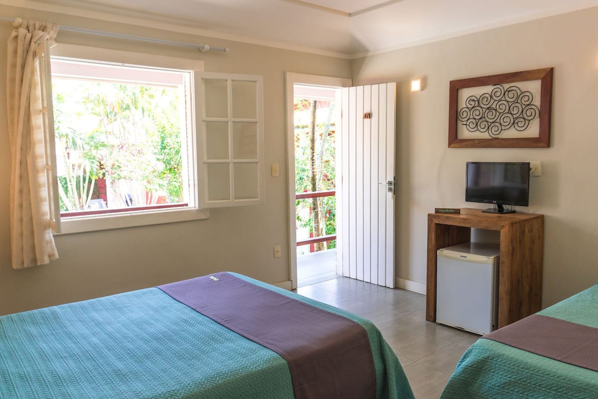 A room with two beds, a TV on a wooden stand, a small fridge, and a window with curtains.