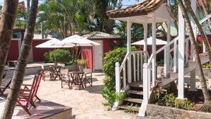 An outdoor patio with stone flooring, white wooden furniture, and umbrellas. - Pousada Tartaruga (Búzios)
