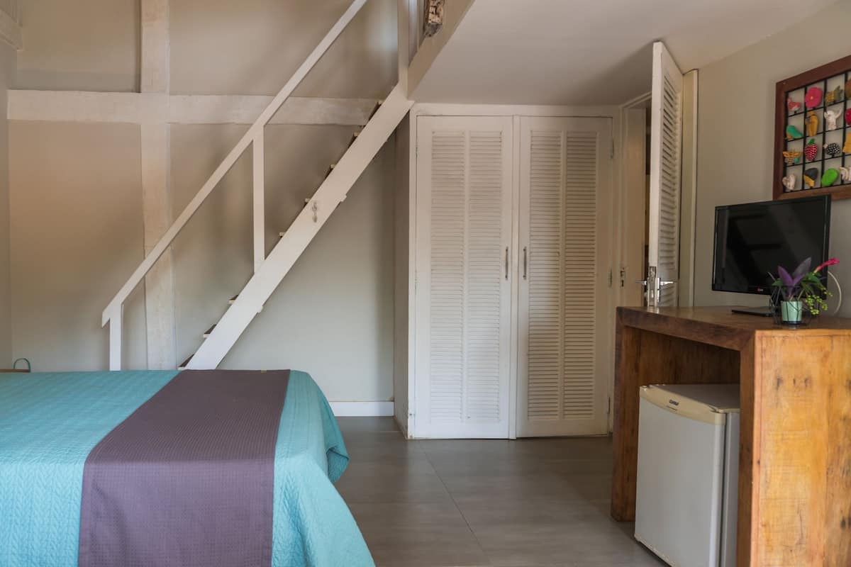 A bedroom with a bed, a desk with a television, a small refrigerator, and a staircase.