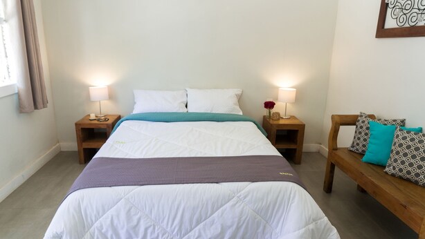 Une chambre à coucher bien aménagée, avec un lit, deux tables de chevet dotées de lampes, un banc avec des coussins et une œuvre d’art accrochée au mur.