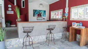 A bar area with a stone floor, red walls, and metal bar stools. There are two bar stools, a wooden table with a sign, and a potted plant. - Pousada Tartaruga (Búzios)