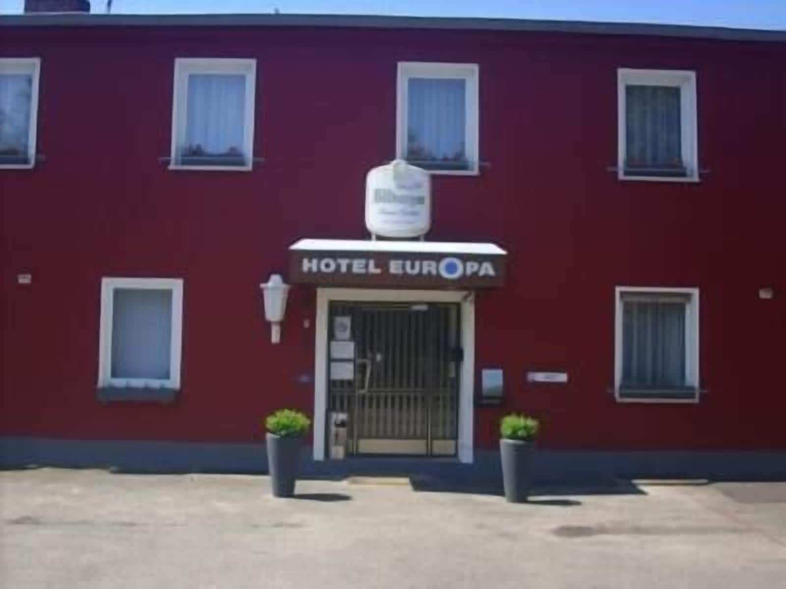 Un bâtiment rouge avec une enseigne indiquant « HÔTEL EUROPA » et une entrée fermée par un portail.