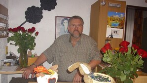 A man seated at a table with a menu, surrounded by red roses and a heart-shaped vase.