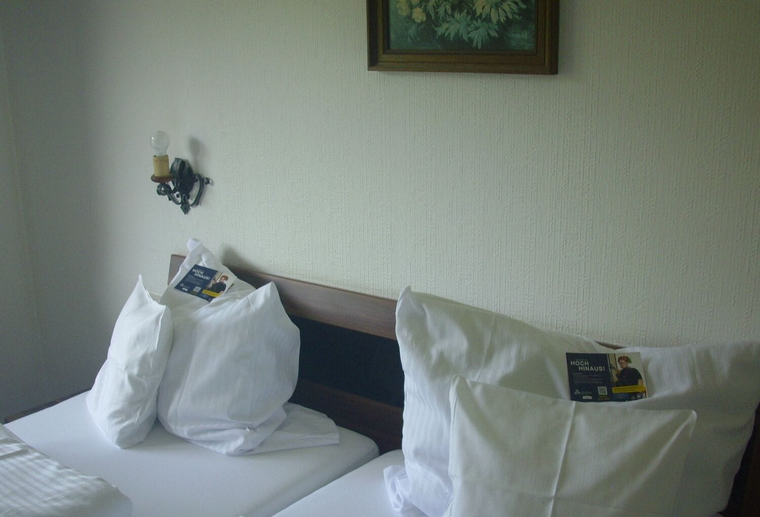 A hotel room with two beds, each with white linens and pillows. There is a framed picture on the wall above the beds.