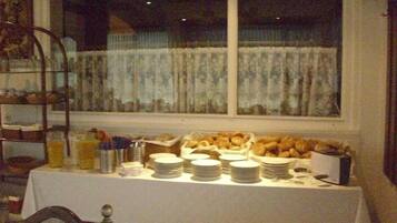 A breakfast buffet setup with plates, bowls, and baskets of pastries on a table.