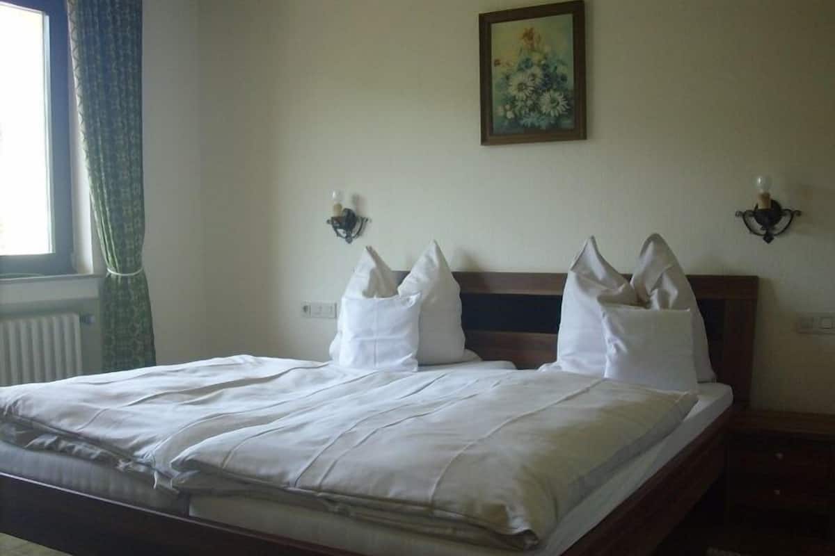 A neatly made bed with white linens in a room with a wooden headboard, a painting on the wall, and a window with curtains.