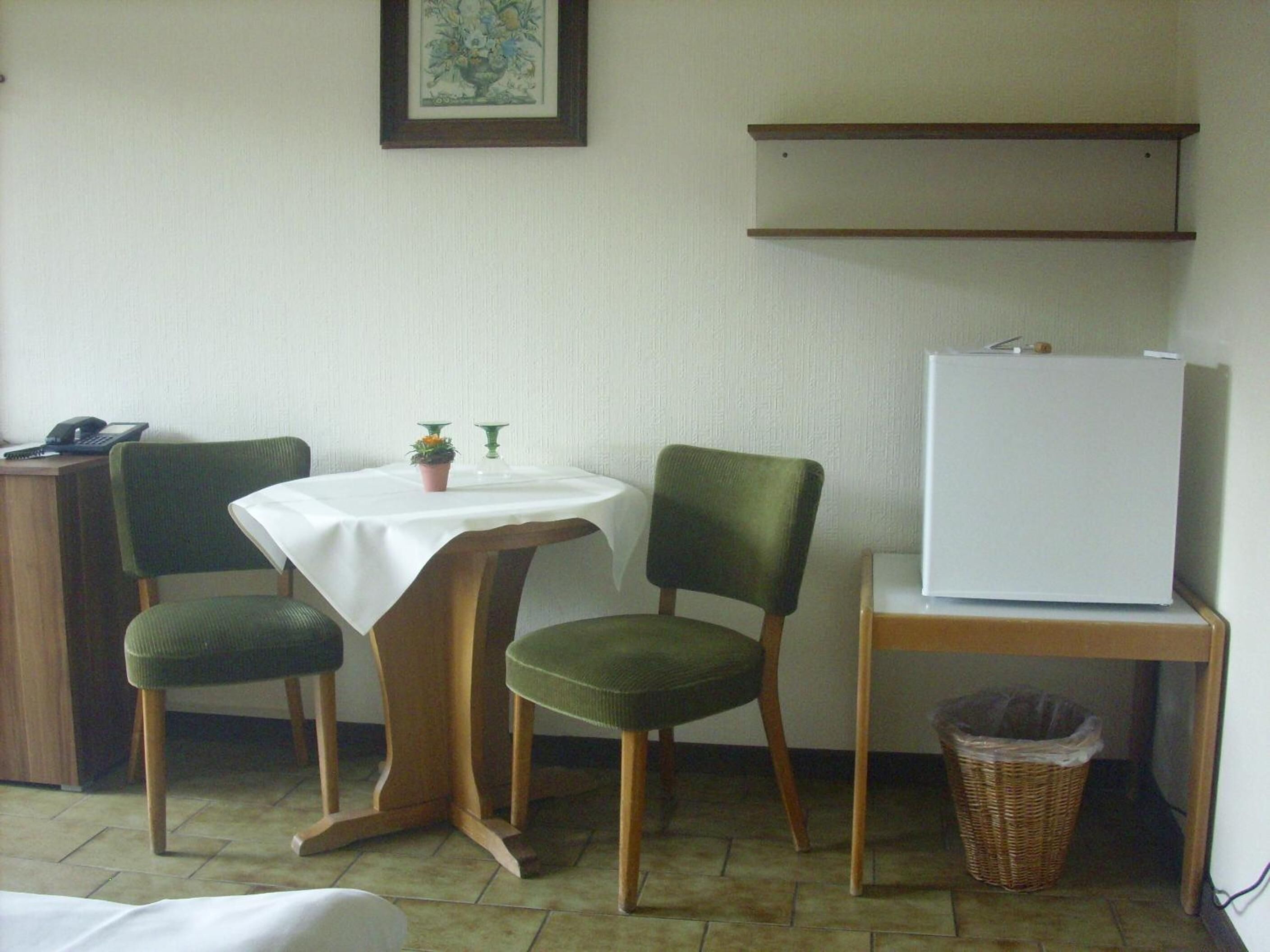 A small room with a table, two chairs, a refrigerator, a trash bin, and a desk with a telephone.