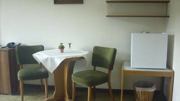 A small room with a table, two chairs, a refrigerator, a trash bin, and a desk with a telephone.