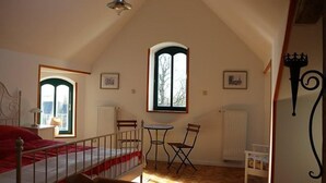 A bedroom with a bed, a chair, a table, and two windows.