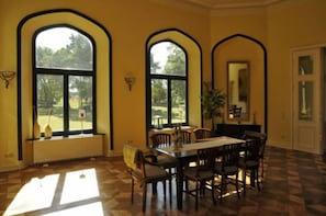 A dining area with a large table and chairs, three arched windows, and a view of the outdoors. - Herrenhaus Alt Vorwerk (Walkendorf)