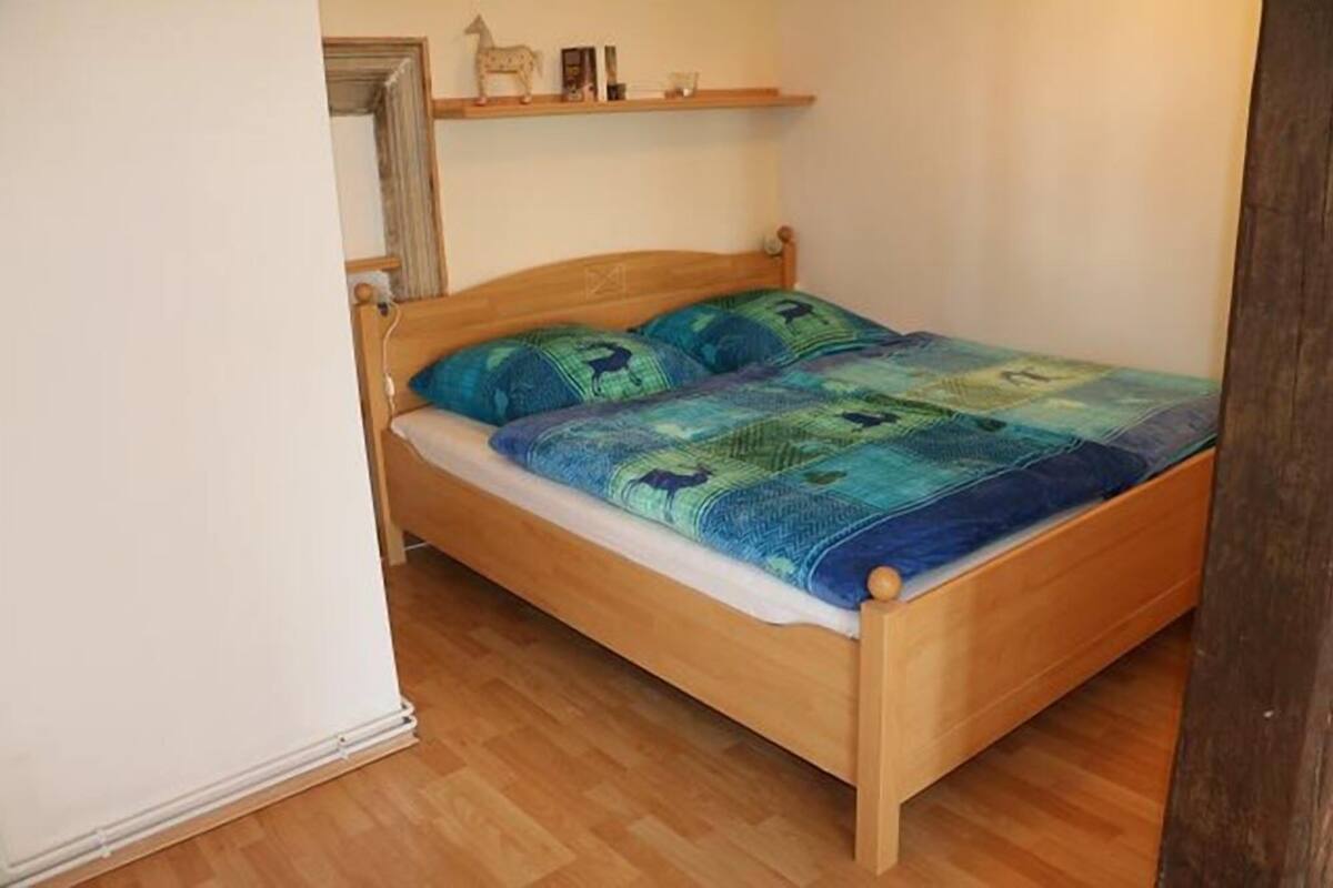 Uma cama de solteiro com estrutura de madeira e colcha acolchoada.