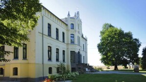 A large, historic building with a symmetrical facade, multiple windows, and a well-maintained lawn with trees.