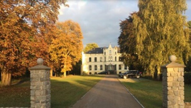A large, stately building with a symmetrical facade, a central entrance, and a driveway leading to the main entrance.