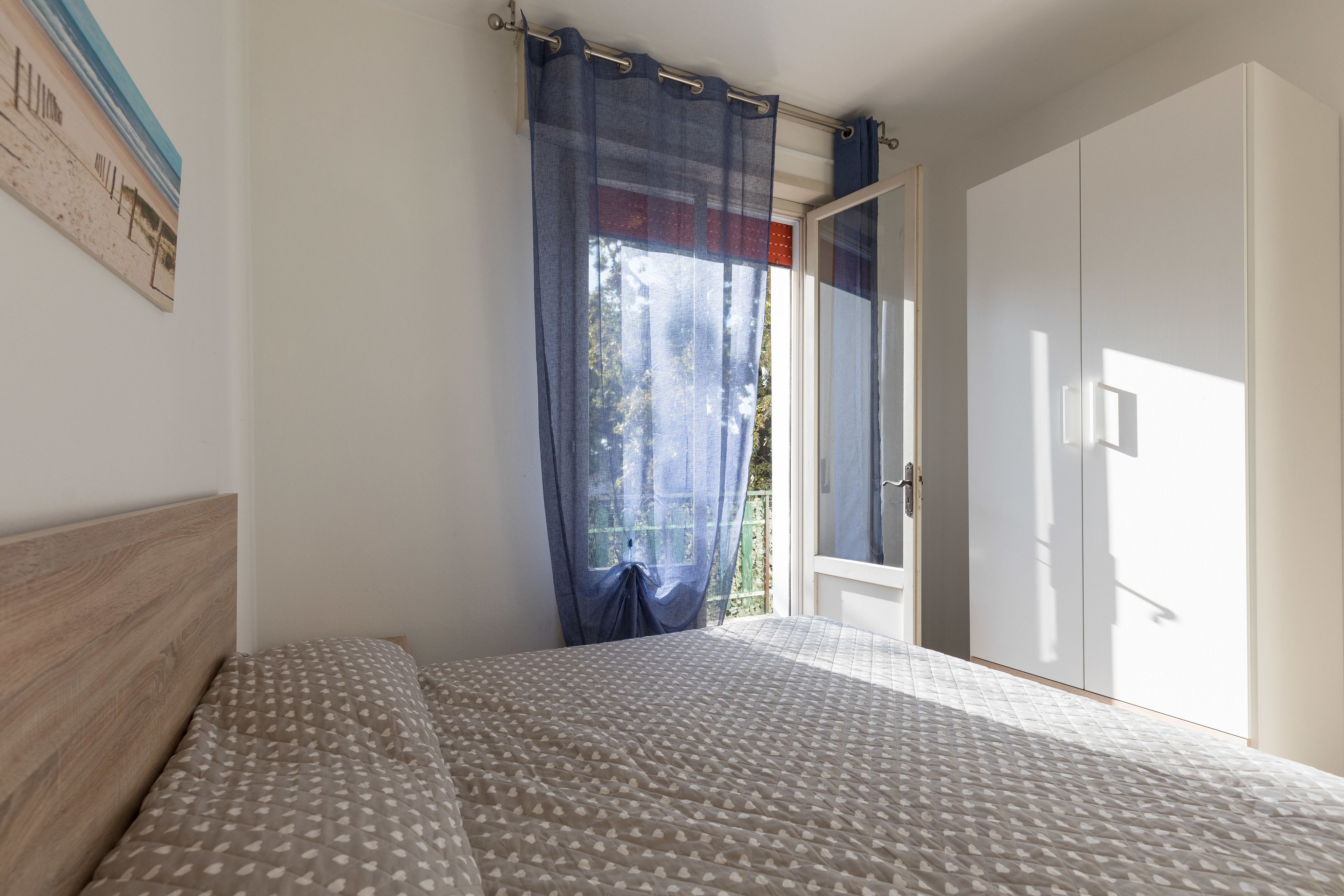 Un dormitorio con cama, ventana con cortinas y armario.
