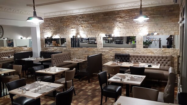 Un restaurant aux murs de pierre, avec des banquettes en cuir et des tables dressées pour le dîner.