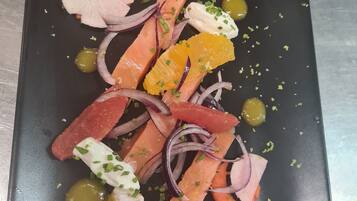 A rectangular black plate with various food items including salmon, pickled vegetables, and garnishes.