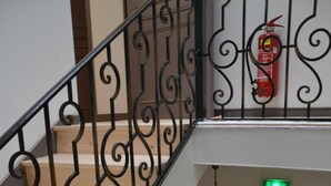 Un escalier orné de rampes noires, un extincteur et un panneau de signalisation verte indiquant la sortie.