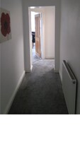 A narrow hallway with a carpeted floor, white walls, and a radiator on the right.