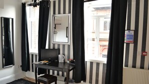 A room with a black and white striped wall, a desk with a computer, a chair, a coffee maker, and a window with black curtains. - The Wrens (Leeds)