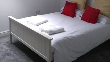 A neatly made bed with white linens and red and beige pillows, a white headboard, and a skylight above.