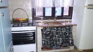 Een kleine keuken met een gasfornuis, een spoelbak en een raam met gordijnen.