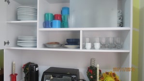 Een keuken met witte planken waarop borden, kommen, bekers en glazen staan. Op het aanrecht staat een broodrooster.