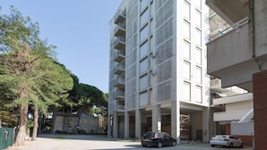 A multi-story building with balconies, a parking area, and trees.