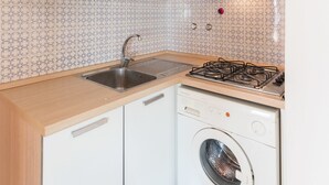 A compact kitchen with white cabinets, a built-in washing machine, and a tiled backsplash.
