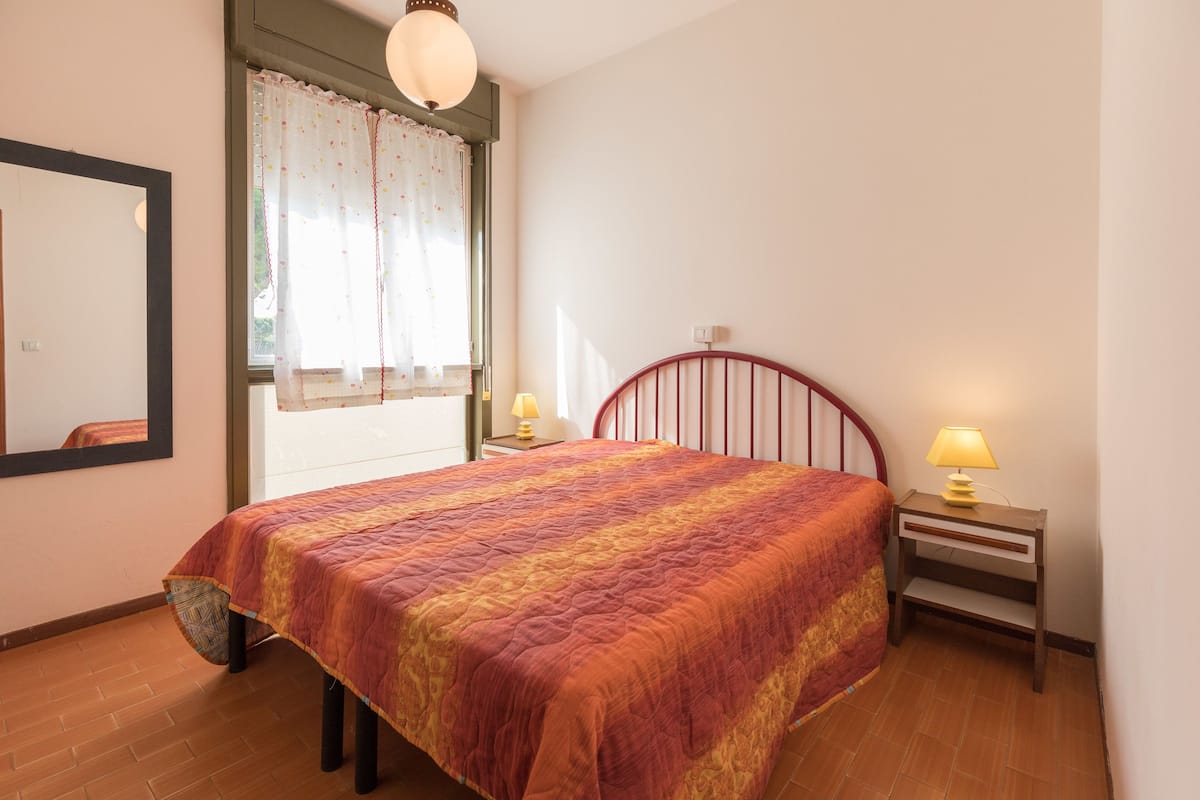 Une chambre à coucher avec un lit, une table de chevet avec une lampe, une fenêtre avec des rideaux et un miroir sur le mur.