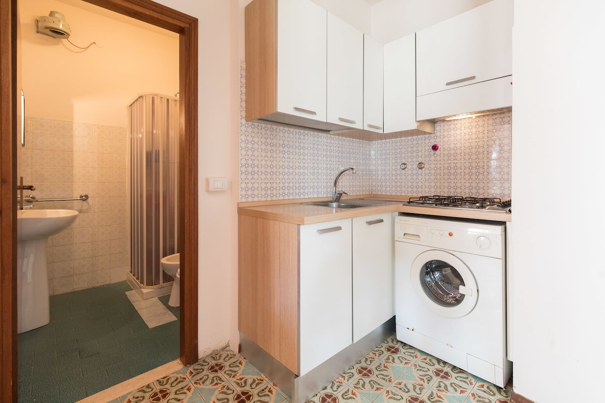 Une cuisine de taille réduite, équipée d’un évier, d’une cuisinière et d’un lave-linge.