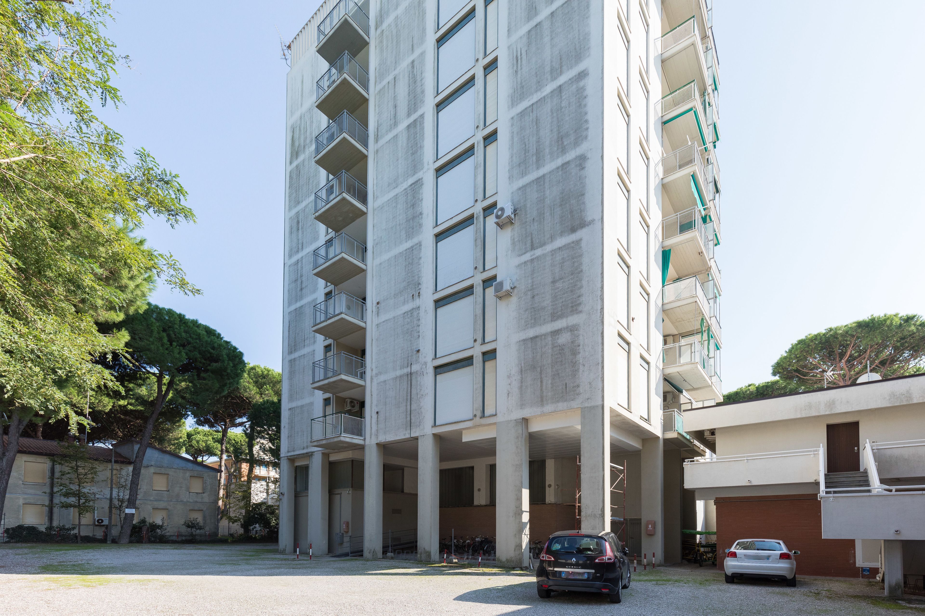 A multi-story building with balconies and a parking area.