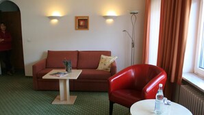 Una habitación con un sofá marrón, una silla roja, una mesita con una revista y una botella de agua.