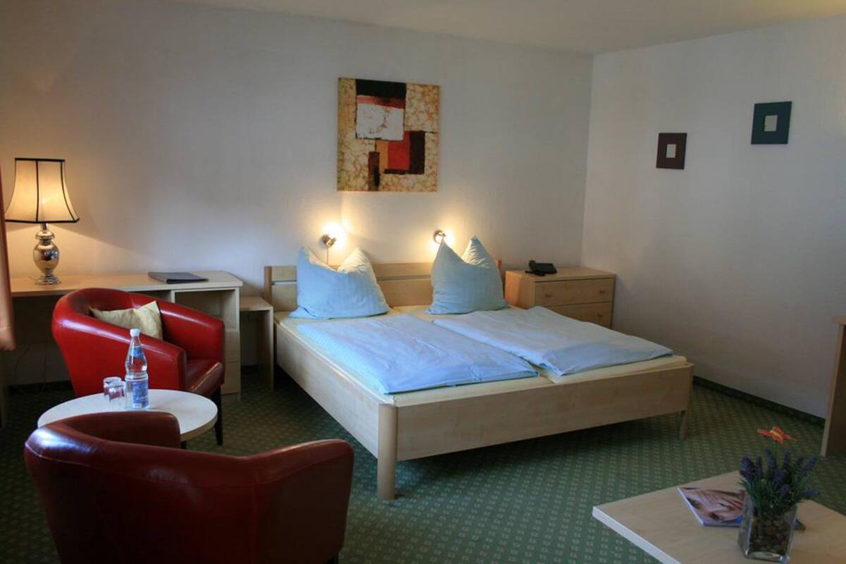 Et hotelværelse med en seng, et skrivebord, en stol og et lille bord med en lampe.