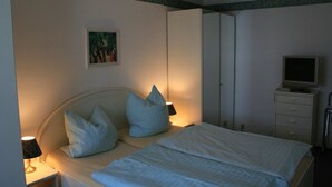 Un dormitorio con cama, almohadas, lámpara de noche, televisor sobre un mueble y armario.