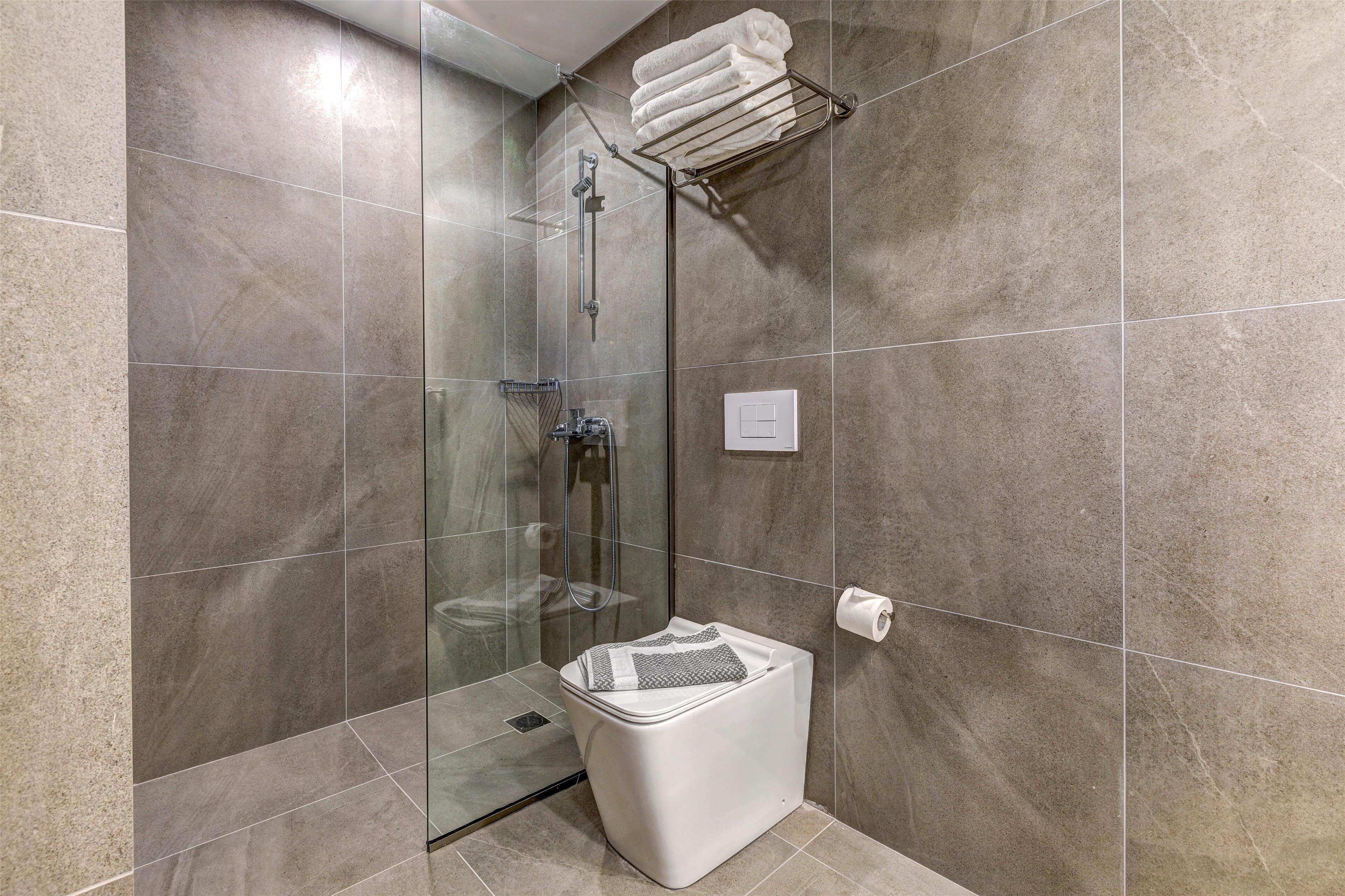 A modern bathroom with a glass-enclosed shower, a white toilet, and a towel rack.