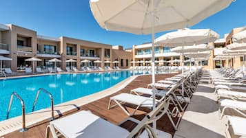 A poolside area with sun loungers and umbrellas, a clear blue pool, and a modern building with balconies.