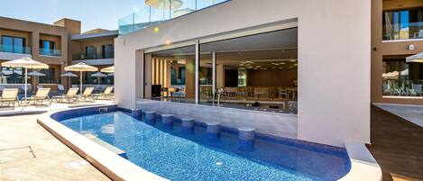 Un hotel moderno con piscina, tumbonas y mobiliario exterior.
