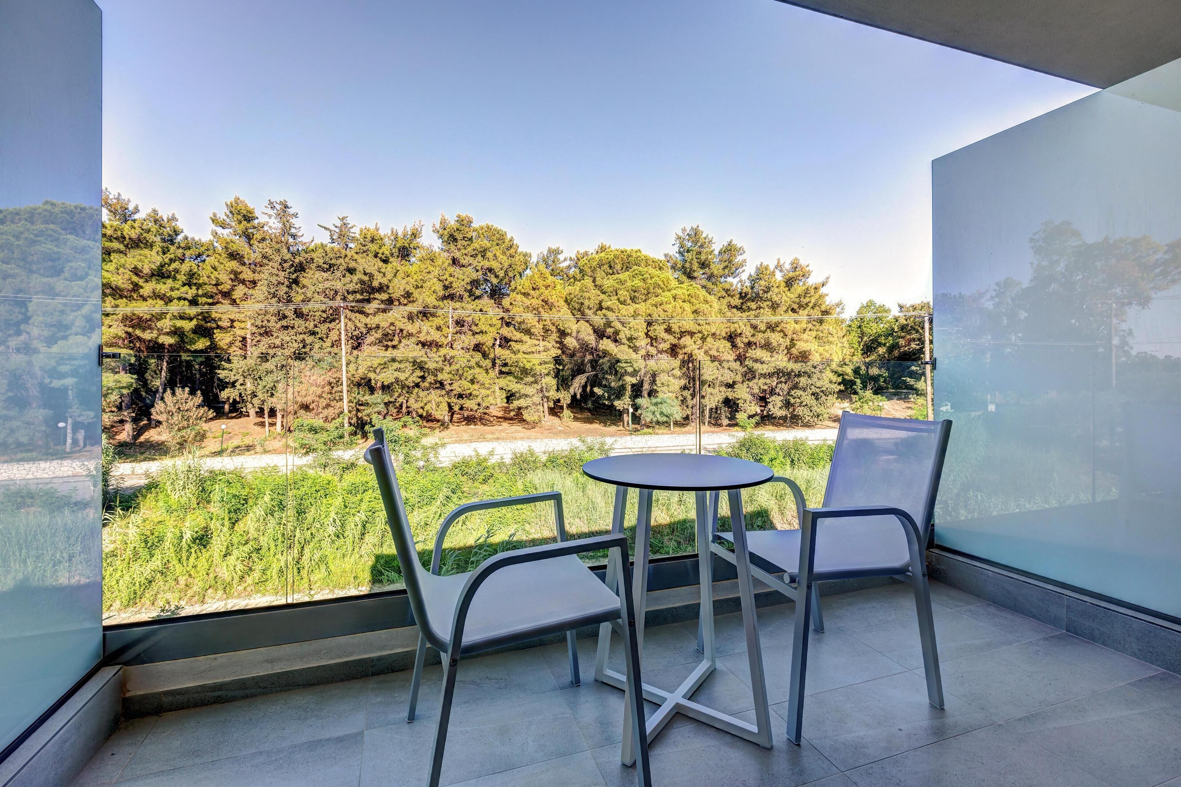 A balcony with a table and chairs, overlooking a forested area.