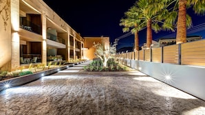 A hotel courtyard with a paved walkway, palm trees, and illuminated balconies. - White Olive Elite Laganas - All Inclusive (Zakynthos)