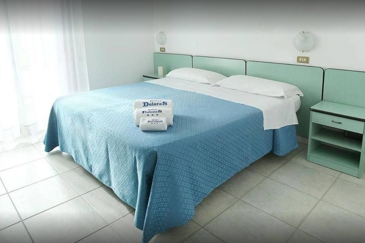 A neatly made bed with a blue bedspread and pillows, a bedside table with a lamp, and a small nightstand with a drawer.