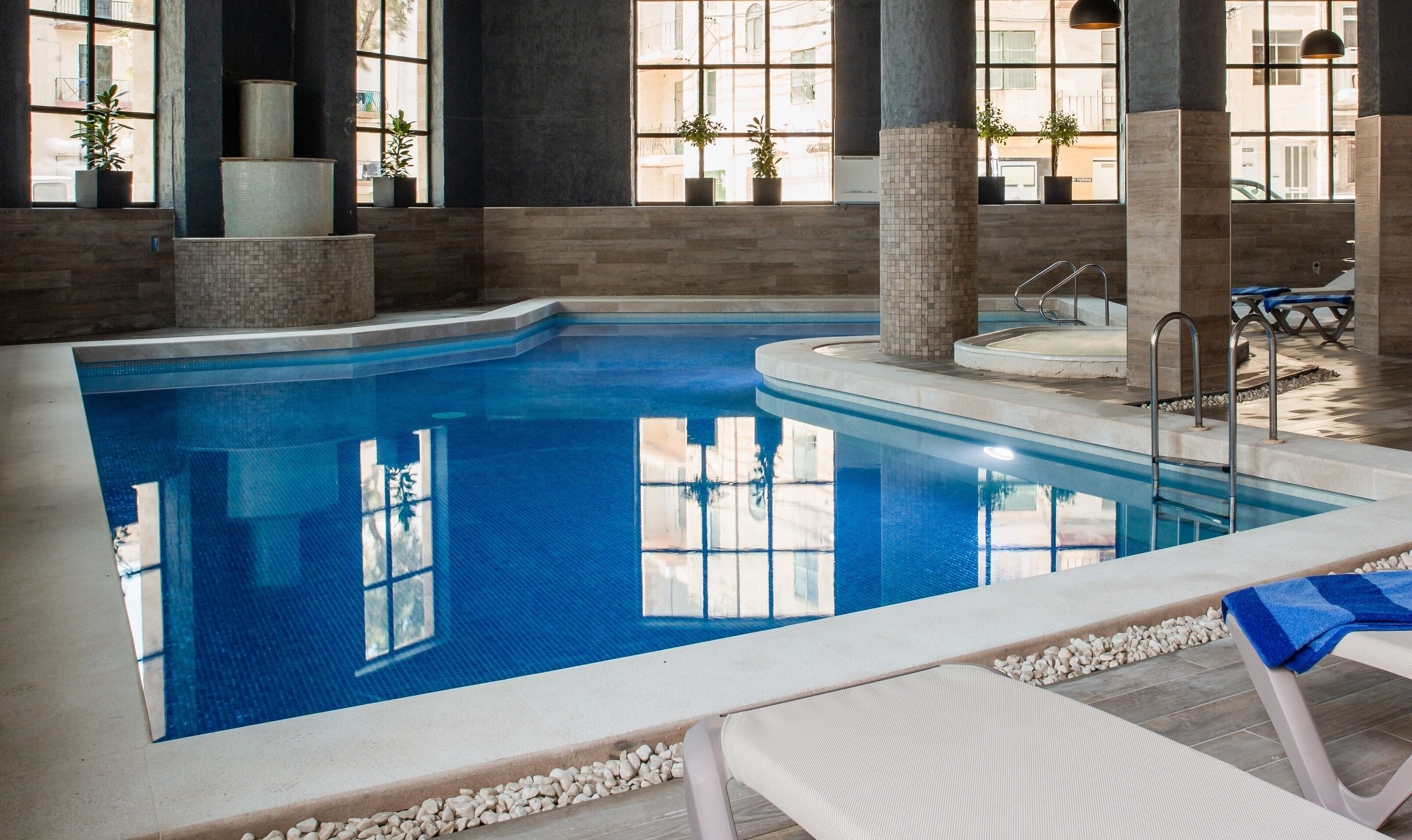 Une piscine intérieure à l’eau d’un bleu cristallin, entourée de murs en pierre et dotée de grandes fenêtres.