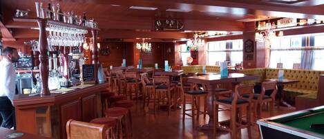 Un área de bar con muebles de madera, mesa de billar y mesa de futbolín.