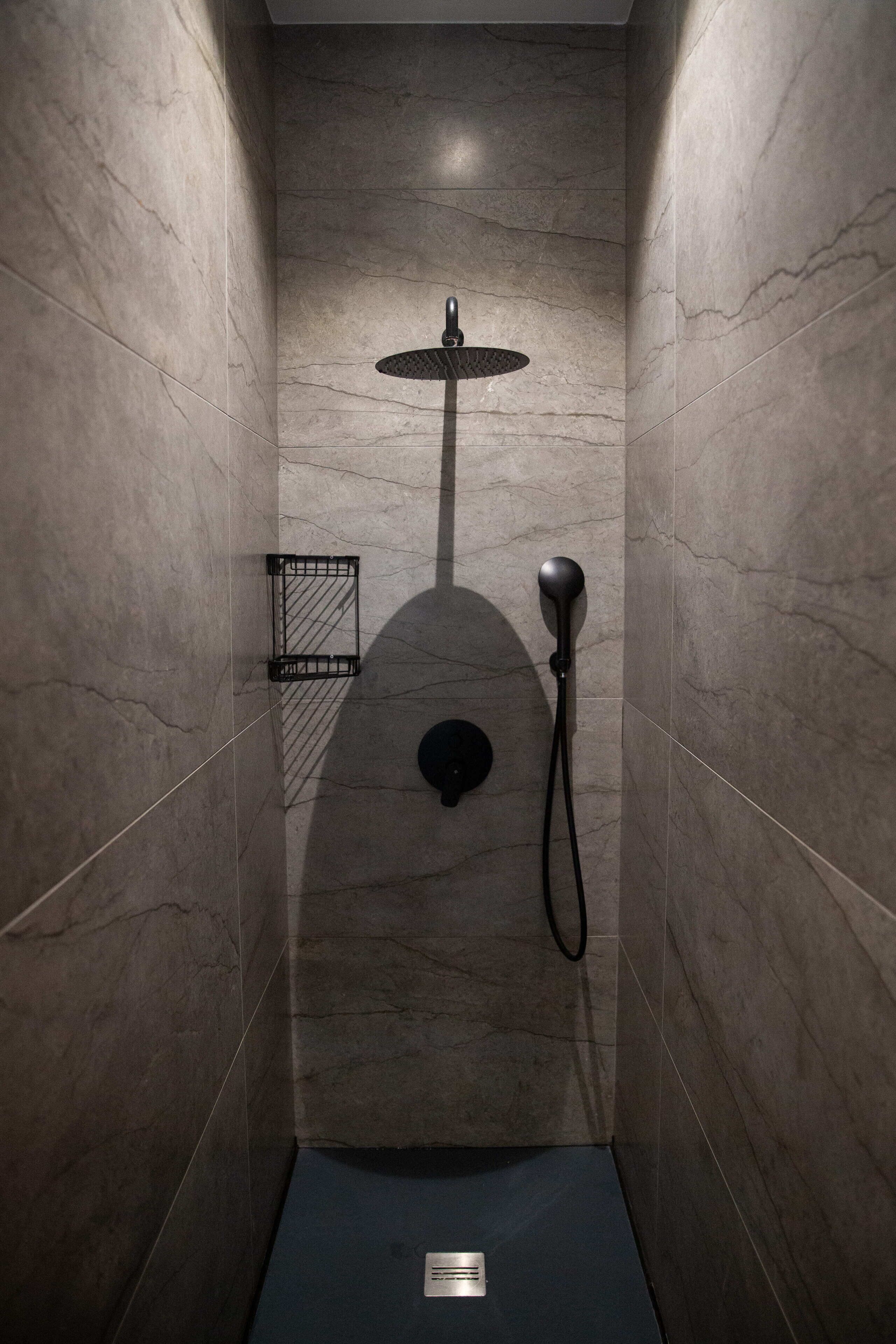 Une douche équipée d’un pommeau de douche à main, d’un robinet mural et d’une petite étagère.