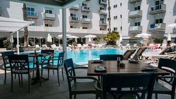 Zona de piscina con sillones reclinables y sombrillas, una mesa de comedor y vistas a la piscina.