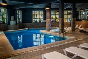 An indoor swimming pool with clear water, surrounded by lounge chairs and a wooden deck. - Pebbles Resort (St. Paul's Bay)
