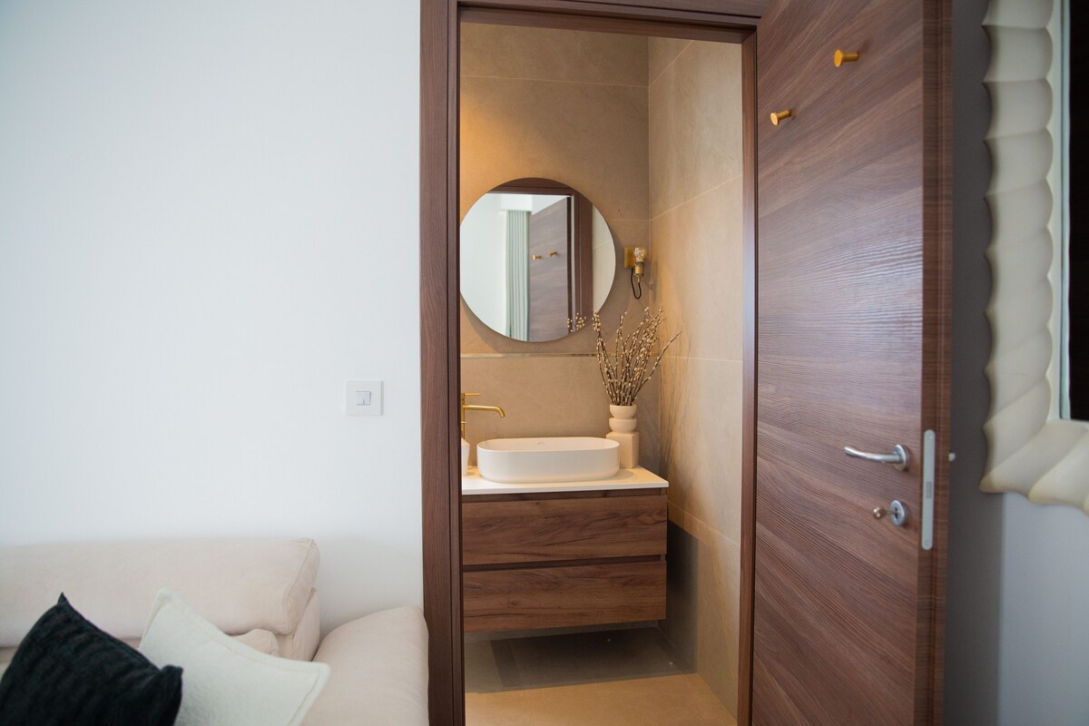 Un baño con tocador de madera, espejo redondo y lavabo blanco.
